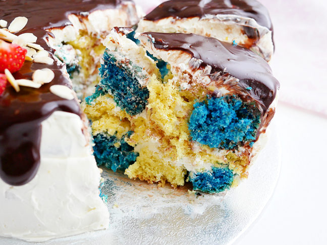 En tårtbit som ser ut som svenska-flaggan dekorerad med smörkräm, choklad och färska bär.
